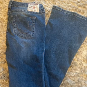 True Religion bootcut jeans blå, stl 28 - Säljer ett par klassiska blå jeans från True Religion i bootcut-modell. Jeansen har ikoniska bakfickor med kontrastsömmar och patch med logga bak i midjan. Tillverkade i jeansmaterial och har en snygg, något utsvängd passform. Helt ny utanprislapp!