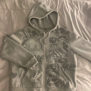 Grå hoodie med tryck och dragkedja - Säljer en grå hoodie med coolt grafiskt tryck framtill med dragkedja.🩶