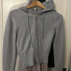 Grå stickad hoodie från Nelly - Mysig grå stickad hoodie från Nelly i storlek S. Tröjan har dragkedja framtill, huva med snörning och bred ribbad mudd i nederkant. Perfekt för lager-på-lager och chill dagar. Långärmad och i mjukt material som känns skönt mot huden. Använd några få gånger 