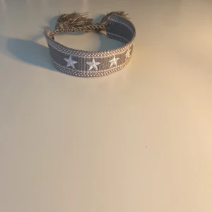 Grått tygarmband med vita stjärnor som är hemmagjort!!! - Snyggt grått armband som jag har gjort ensam hemma!!! Med lite hjälp från min mamma… Säljer ett för 100kr och två för 150kr!! Skriv för mer frågor!🙂