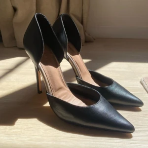 Svarta pumps från Blondish i skinn - Snygga svarta pumps från Blondish i äkta skinn med spetsig tå och hög klack. Modellen har öppen insida och elegant siluett, perfekt för dig som gillar stilrena klackar. Storlek 40, tillverkade i Spanien. Säljer då jag fick för stor storlek. Endast använda en gång. Lägg ett bud🖤10 cm