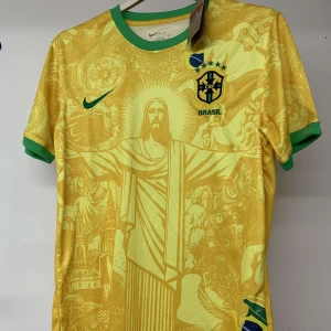 Brasilien fotbollströja Nike gul/grön - Snygg Brasilien fotbollströja från Nike i gult med gröna detaljer vid krage och ärmslut. Framsidan har ett unikt grafiskt mönster med Kristusstatyn och brasilianska motiv. Broderat CBF-märke och Nike-logga på bröstet. Tillverkad i lätt och ventilerande material.