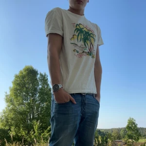 Vit t-shirt Polo Ralph Lauren - Vit t-shirt från Polo Ralph Lauren med färgglatt palmtryck och texten 'Paradise Est 1967' på bröstet. Klassisk passform och mjuk bomullskvalitet. Perfekt för dig som gillar chill och tropiska vibes. Nypris 1600. Top kvale och condition!!🤞 Priset går alltid att ändras på😁