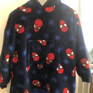 Mörkblå Spiderman hoodie fleece - Supermysig mörkblå hoodie med Spiderman-tryck över hela tröjan. Tröjan har huva, stor magficka och är gjord i mjuk fleece. Perfekt för dig som älskar Marvel och vill ha något riktigt chill att hänga i hemma. Långärmad och loose fit. Använd 1 gång och inget mer köpte den i usa