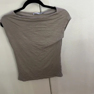 Beige topp från 157, XS - En enkel och stilren beige topp från 157 i storlek XS. Toppen har en rak och loose passform med korta ärmar och rundad hals. Materialet är mjukt och känns som bomull, perfekt för en chill look. Snygg att matcha med jeans eller kjol.