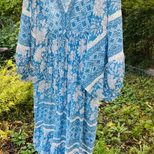 Blå och vit indiska -klänning med blommor - Superfin långklänning i boho-stil med blått och vitt blommönster och geometriska detaljer. Klänningen har v-ringning, vida långa ärmar och ett luftigt fall. Perfekt för dig som gillar en avslappnad och romantisk vibe. Väldig rymlig s-L