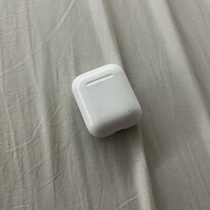 AirPods (2nd generation) - Apple AirPods (2nd gen) med laddningsetui. Fungerar bra, laddningsindikator lyser. Viss yttre slitage och smuts synligt på etuiet och insidan av locket, men inget som påverkar funktionen. Perfekt för trådlös musik och samtal. SAKNAS EN PODD!