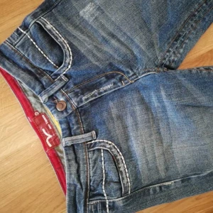 Blå bootcut jeans med kontrastsömmar - Snygga blå jeans från Replay med bootcut-modell och markerade vita kontrastsömmar. Jeansen har coola detaljer på bakfickorna och en röd insida i midjan. Klassisk femficksdesign. Säljer då de är lite stora på mig💕