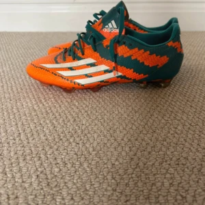Adidas F50 adizero messi pibe de barr10 FG - Säljer ett par Adidas fotbollsskor med Messi-logga. Skorna är orange och gröna med vita detaljer och har ett coolt, sicksack-mönster. De har snörning, platt sula med dobbar och är tillverkade i syntetmaterial. No box. No bag. Hence why a very rare pair of trainers I’m selling for an absolute steal. Will take offers. 