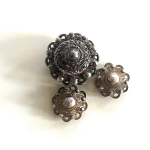 Antika Holländska Zeeuwse Silverknappar-Mycket fint skick! - Nu kan du bli ägare av dessa vackra holländska silverknapparna som tillverkats någon gång mellan 1879-1910. De är tillverkade speciellt för en holländsk folkdräkt men idag finns det många som gör smycken av dem då de är högt värderade, speciellt flera i en serie. Finns märkning på största knappen med någon sorts triangel (jag ser inte vad det är exakt) och sedan JB          Mått:Större knapp 2 cm i diameter, H 1,5 cm 2 mindre knappar 1,4 cm i diameter, H 0,8 cm Vikt 6,9 gram för alla tre