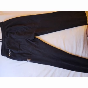 Svarta Hoodrich mjukisbyxor med patchar - Säljer för ja typ alldrig använt. Svarta mjukisbyxor från Hoodrich med broderade patchar och stor vit logga framtill. Byxorna har snörning i midjan och är gjorda i mjukt bomullsmaterial. Snygg röd H-detalj och flera coola märken på framsidan ger streetkänsla. 