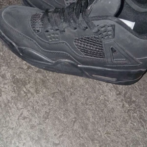 Nike Air Jordan 4 Triple Black - Säljer ett par helsvarta Nike Air Jordan 4 med klassisk meshpanel på sidorna, Jumpman-logga på plösen och robust mocka över hela skon. Snygga detaljer med svarta snören och ikoniska plastdetaljer vid snörningen. Perfekta för dig som gillar stilrena sneakers och gråa båda för 1000