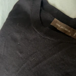 Mörk marinblå merinoull tröjan, Oscar Jacobson  - En klassisk svart stickad tröja från Oscar Jacobson, tillverkad i Italien. Tröjan har rund halsringning, ribbade muddar och lång ärm. Perfekt för dig som gillar stilrena och tidlösa plagg med en snygg passform.