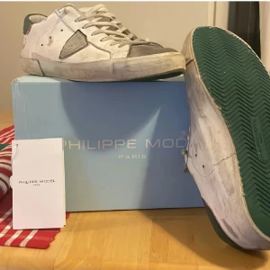 Vita Philippe Model skor  - Säljer nu mer mina Snygga vita sneakers från Philippe Model som jag har använd en sommar med gröna detaljer på hälen och gröna sulor. Skorna har snörning, rund tå och är tillverkade i skinn. Perfekta för dig som vill ha feta och snygga skor| bara att skriva vid minsa fundering eller prisförslag💭| skorna är också väldigt lätt tvättade, har tävättat dom nån gång och får dom som nya😊👍🏻