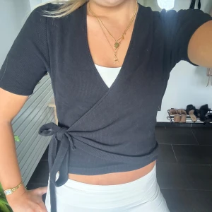 Svart omlottopp från Apart Impressions - Svart omlottopp som är kortärmad från Apart Impressions med knytning! 
