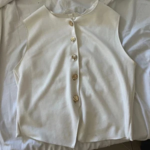 Vit topp med guldknappar - Vit topp med guldknappar i strl S från H&M. Använd en gång och är i mycket bra skick!