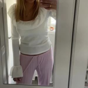 Vit blus med volangkrage och trumpetärm - Supersöt vit blus med stor volangkrage och långa trumpetärmar. Sitter tajt över kroppen och har en lätt ribbad struktur. Perfekt för dig som gillar romantiska detaljer och vill sticka ut lite extra.