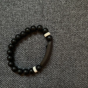 Svart pärlarmband med vita detaljer  - Stilrent armband med svarta runda pärlor och två vita detaljer. Perfekt accessoar för en clean look och passar till det mesta. Elastiskt band gör det enkelt att ta på och av.