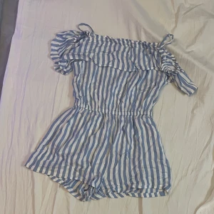 Blåvit randig offshoulder dress - Supersöt kort dress med blå och vita ränder, offshoulder-modell med volang upptill och resår i midjan. Perfekt för varma dagar och ger en fräsch sommarkänsla. Lätt och luftig, passar dig som gillar en avslappnad men trendig stil.