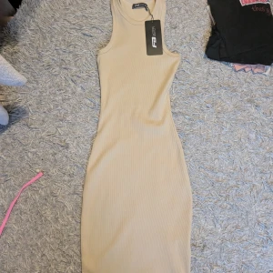 Beige ribbad kortklänning - Supersnygg beige ribbad klänning. Modellen är ärmlös med rund hals och figurnära passform som framhäver siluetten. Perfekt för dig som gillar stilrena och enkla plagg med en modern touch.