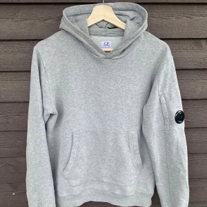 Grå hoodie C.P. Company 12y - Snygg grå hoodie från C.P. Company med klassisk huva och magficka. Ärmen har den ikoniska svarta linsen med logga. Mjuk bomullskänsla och relaxed fit. Storlek: 12y, ca 160. Nypris 1999kr. Hör av dig om du har några frågor elr liknande🙌