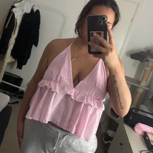 Ljusrosa volangig linnetopp - Supersöt ljusrosa linnetopp med volanger och djup v-ringning. Toppen är ärmlös och knyts i nacken för en halterneck-look. 