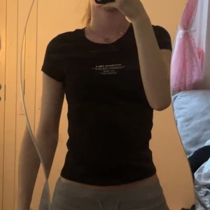 Svart topp med tryck från H&M Divided XS - Svart kortärmad topp från H&M Divided i storlek XS. Toppen har ett vitt futuristiskt tryck på bröstet. Figurnära passform och rund halsringning. Perfekt för en cool och modern look.