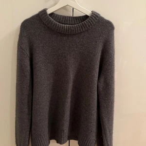 Mörkgrå stickad tröja från Lisa Yang - Mysig mörkgrå stickad tröja från Lisa Yang med rund halsringning och ribbade muddar. Perfekt för lager-på-lager och chill dagar. Tröjan har en klassisk, enkel design som funkar till allt och är tillverkad i ett mjukt material.