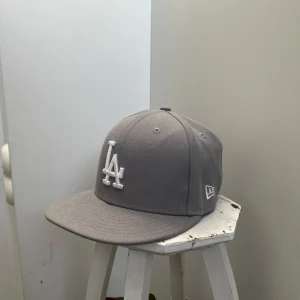 Grå LA-keps New Era  - Snygg grå keps från New Era 59FIFTY med LA-logga broderad framtill i vitt. Klassisk rak skärm. Perfekt till sommaren och i princip oanvänd. Bara skriv vid frågor eller fler bilder