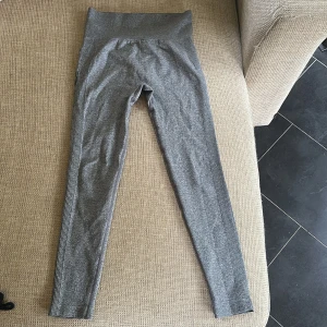 Grå höga seamless leggings - Gråa seamless leggings med hög midja och ribbade detaljer längs sidorna. Materialet är stretchigt och mjukt, perfekt för träning eller chill. Baksidan har diskret scrunch-effekt för extra form. Snygg och enkel design som passar till allt.
