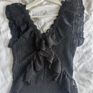 Svart spetsblus från zara - Supersnygg svart blus med spetsdetaljer och volanger längs axlar och bröst. Blusen har en v-ringad hals och är ärmlös, vilket ger en cool och feminin vibe. Perfekt för dig som gillar detaljer och vill sticka ut lite extra. Från zara