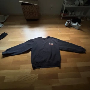 Svart NYC sweatshirt med tryck - Cool svart sweatshirt med tryck på bröstet där det står 'NYC' och stort tryck på ryggen med texten 'Brooklyn New York City USA'. Tröjan har rund hals och långa ärmar, perfekt för en streetstyle-look.