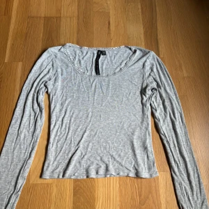 Grå långärmad topp från lager 157 - En enkel och stilren grå långärmad topp från lager 157. Modellen har rundad halsringning med en diskret spetskant och är tillverkad i mjuk bomullsblandning. Perfekt att matcha med jeans eller kjol för en avslappnad look.