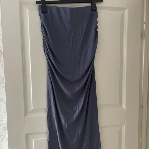 Mörkblå långkjol med drapering - Säljer en stilren mörkblå långkjol med snygg drapering på ena sidan. Kjolen har en rak passform och är tillverkad i ett mjukt, lätt material som faller fint längs kroppen. Perfekt för dig som gillar minimalistisk och trendig stil.