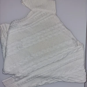 Stickad oneshoulder-tröja Therese L x  NA-KD  - Supersnygg vit stickad tröja från Therese Lindgren for NA-KD. Tröjan har ett unikt oneshoulder-snitt med hög ribbad krage och flätstickat mönster. För dig som vill sticka ut med en trendig och mysig look.