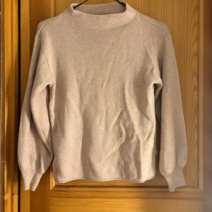 Beige stickad tröja från Dobber - En stilren beige stickad tröja från Dobber i storlek XS. Tröjan har en högre halsringning och långa ärmar med ribbade muddar. Perfekt för lager-på-lager och enkel att matcha med dina favoritjeans eller kjol.