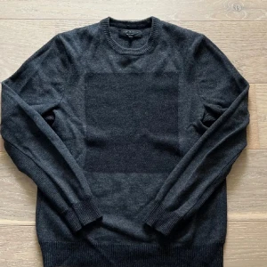 Mörkgrå stickad tröja från Rag & Bone - Snygg mörkgrå stickad tröja från Rag & Bone med rund halsringning och ribbade muddar. Tröjan har en diskret rutig effekt framtill och är tillverkad i mjukt material som passar perfekt för kyligare dagar.