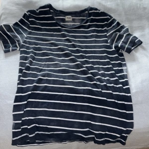 Randig t-shirt från Acne, marinblå - Snygg t-shirt från Acne i marinblått med vita horisontella ränder. Klassisk rund hals och korta ärmar. Mjuk bomullskvalitet som känns skön mot huden. Perfekt för dig som gillar stilrena och enkla plagg med en modern touch.