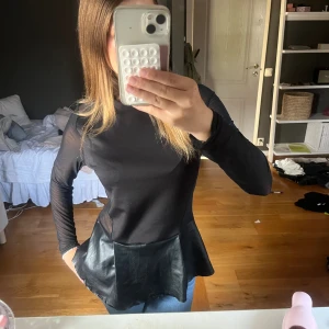 Svart långärmad topp med skinnvolang - Säljer en svart långärmad topp med transparenta meshärmar och rygg. Toppen har en snygg volang nertill i fejkskinn som ger en cool kontrast till resten av plagget. Passformen är normal och toppen är perfekt för dig som gillar unika detaljer. Kommer inte ihåg vart jag köpte eller beställde o den saknar lapp! Passar mig som är XS kanske lite ytterst stor passar S med!