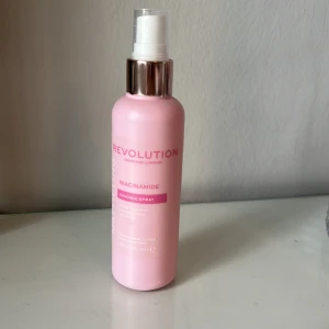 Revolution Niacinamide Essence Spray - Fräsch rosa face mist från Revolution med niacinamide. Kommer i en smidig sprayflaska med vit pump och silverdetalj. Perfekt för att ge huden en återfuktande boost och matt finish. Vegansk och cruelty free.