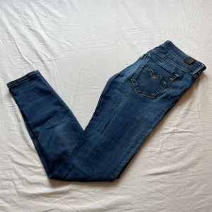 Blå Replay jeans  - Snygga blå jeans från Replay med klassisk femficksdesign och slim fit. Jeansen har tydliga Replay-detaljer vid fickan och läderpatch bak i midjan. Materialet är slitstarkt denim i bomull och passformen är normal med raka ben.