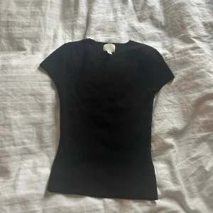 Svart kortärmad topp från H&M - En svart, enkel och tight topp från H&M med rund halsringning och korta ärmar. Perfekt basplagg i garderoben, lätt att matcha med allt. Tillverkad i mjuk bomull för en bekväm känsla hela dagen.