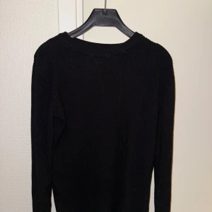 Svart stickad tröja från C - En svart, ribbstickad tröja från Cubus i storlek 146/152. Tröjan har lång ärm och klassisk rund halsringning. Perfekt för dig som gillar en enkel och stilren look.