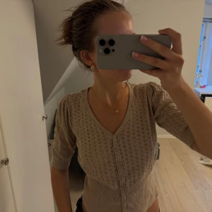 Beige kofta från KappAhl XS - Supersöt beige kofta från KappAhl i stickat material. Koftan har v-ringning, kortare ärmar och fina knappar framtill. Detaljerad med ett diskret hålmönster som ger en extra touch. Perfekt att slänga på sig över ett linne / t-shirt eller bara som en vardaglig tröja! Säljer för att den ej kommer till användning