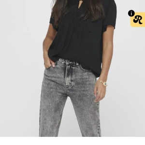 Svart blus med knyt från JDY - Svart blus från JDY i storlek 34 med korta ärmar, diskret prickigt mönster och volangkantad krage. Blusen har knytband vid halsen och en lös, luftig passform. Perfekt att styla med jeans eller kjol för en trendig look.