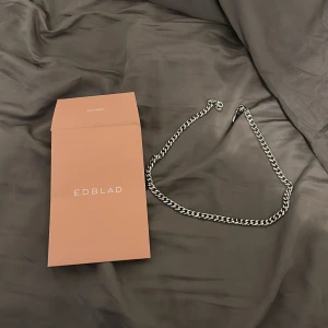 Silverfärgat kedjehalsband från Edblad - Stilrent halsband från Edblad i silverfärg med klassisk kedjelänk. Halsbandet har en snygg, tidlös design som passar perfekt till olika stilar. Levereras i originalförpackning från Edblad. knappt använd! 