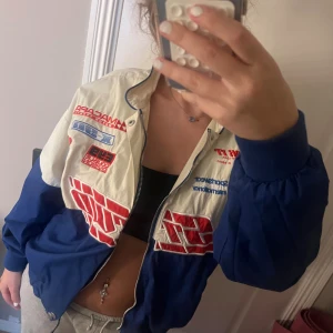 Blåvit racing vindjacka från Pull&Bear - Snygg blå och vit vindjacka från Pull&Bear med racing-inspirerade tryck och broderier i rött och blått. Jackan har dragkedja, ståkrage och muddar vid ärmslut och midja. Perfekt för dig som gillar sportig och retro stil! :) ⚠️ORIGINAL PRIS: 800kr ⚠️