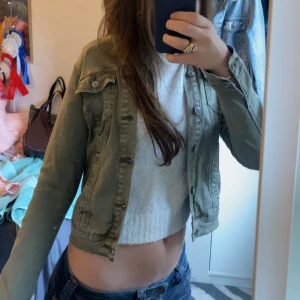 Olivgrön jeansjacka med knappar - Snygg olivgrön jeansjacka med klassisk krage, bröstfickor med lock och knappar framtill. Jackan har en croppad passform och långa ärmar.Säljer för den är för liten för mig 