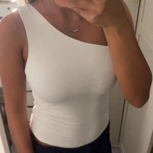 Vit one shoulder topp Gina Tricot - Säljer en vit one shoulder topp från Gina Tricot i storlek S. Toppens enkla och stilrena design gör den lätt att matcha och den är tillverkad i ett mjukt och stretchigt material som sitter tight mot kroppen. Perfekt för dig som gillar minimalistisk stil.