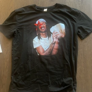 Svart t-shirt - King Von - Svart t-shirt King Von print på bröstet som föreställer en person med tatueringar och keps som håller en bunt sedlar. Klassisk passform och rund hals. 